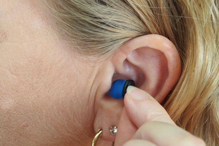 Woman inserts earplugs into her ears.