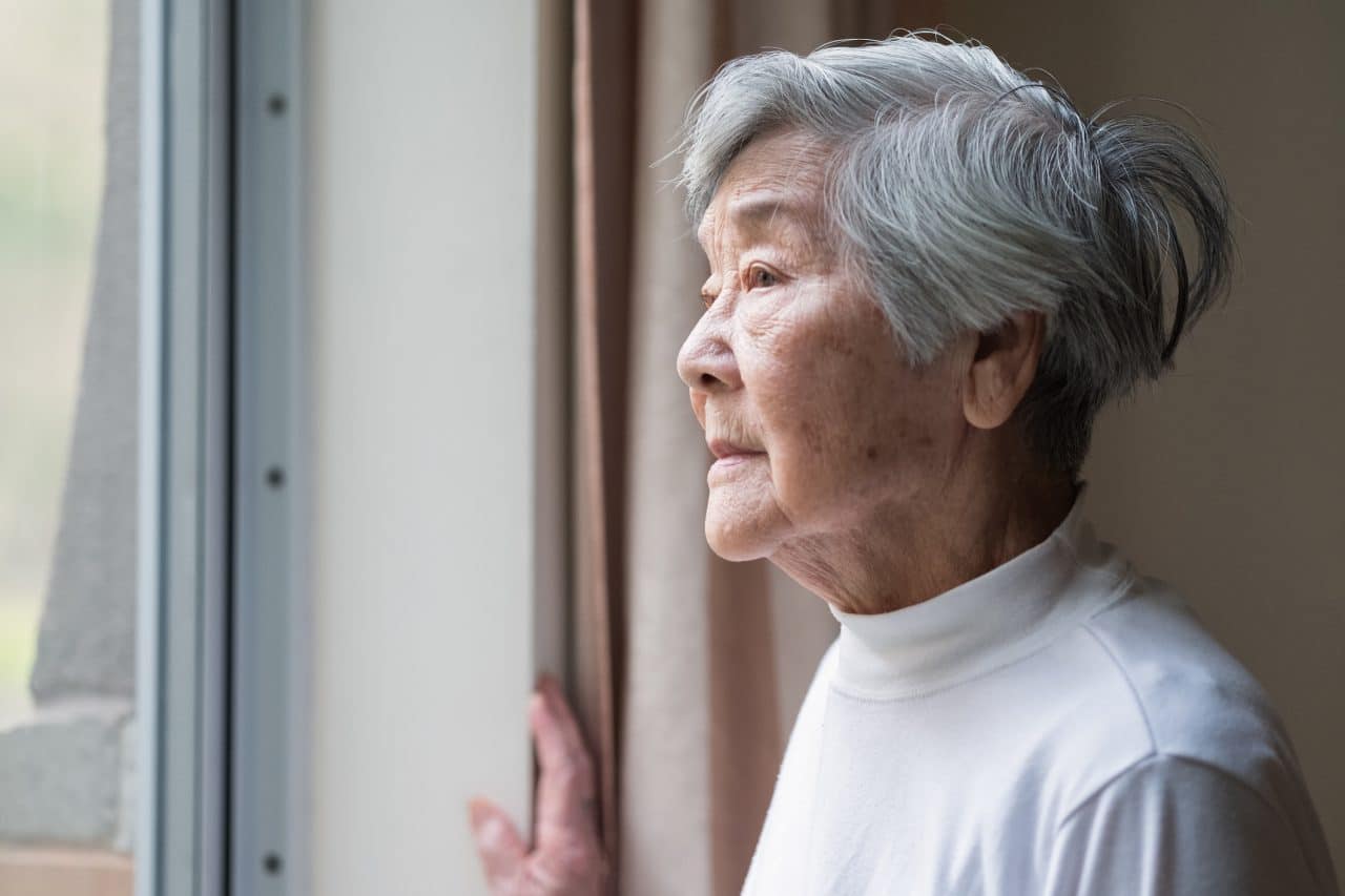 Older woman looking outside window.