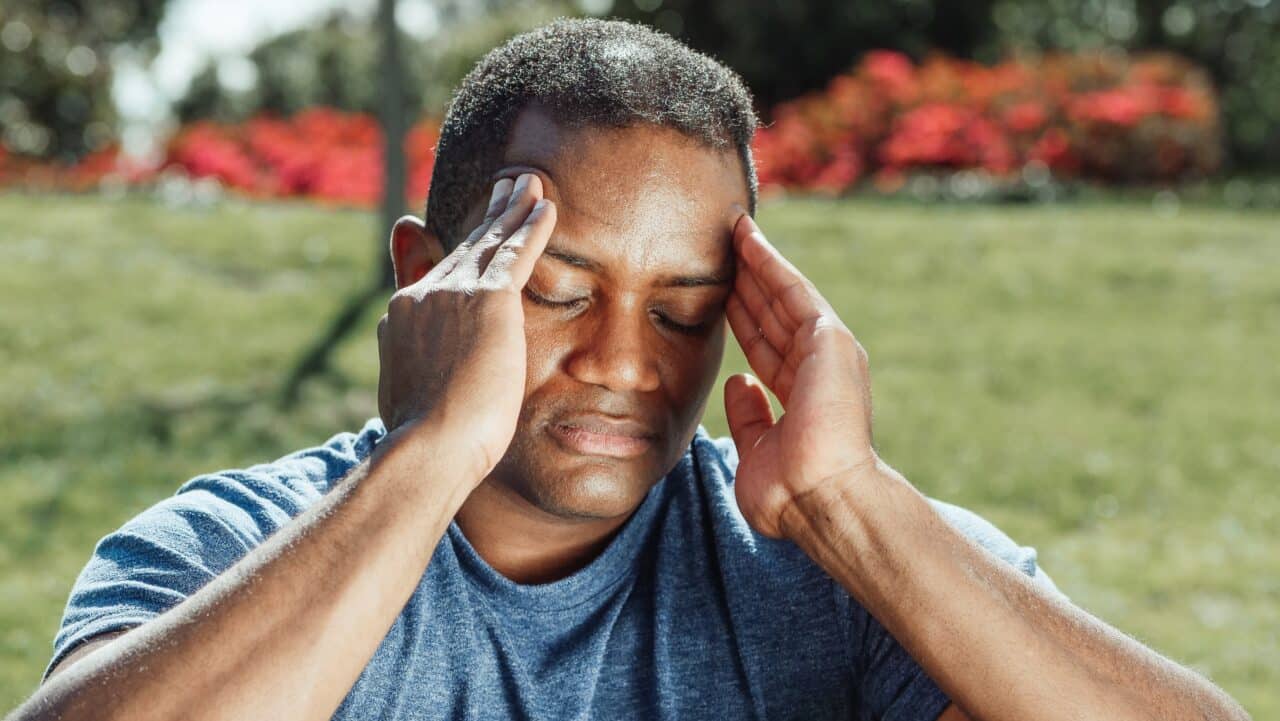 Young man experiencing a migraine outside.