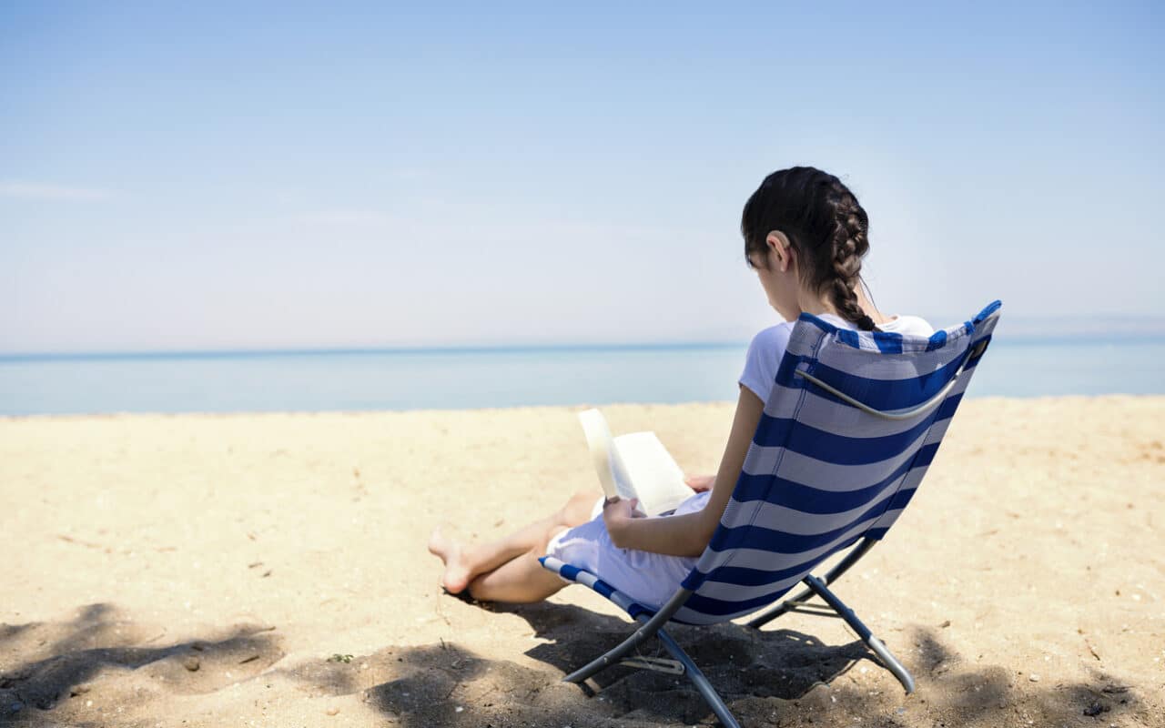 Woman wearing a hearing aid reading on the beach.